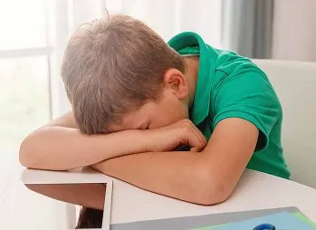 Menino com a cabeça apoiada na carteira da escola.