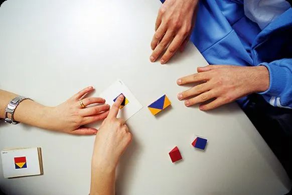 Mãos sobre a mesa manipulando peças coloridas durante a aplicação de um teste neuropsicológico.