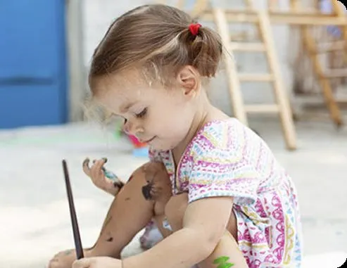 Criança pequena pintando, concentrada na atividade.